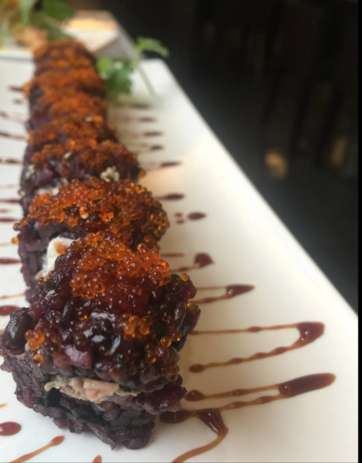 Rotoli di sushi piccanti conditi con salsa scura, serviti su un piatto rettangolare bianco.