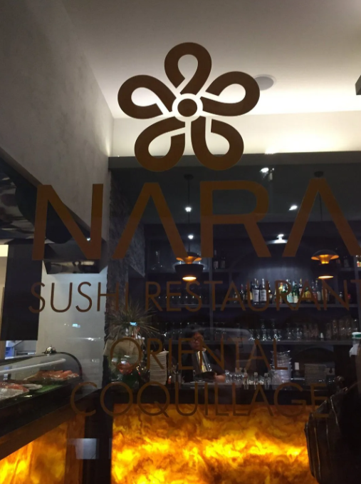 Ingresso del ristorante di sushi NARA con logo sulla porta in vetro e calda illuminazione arancione all'interno.