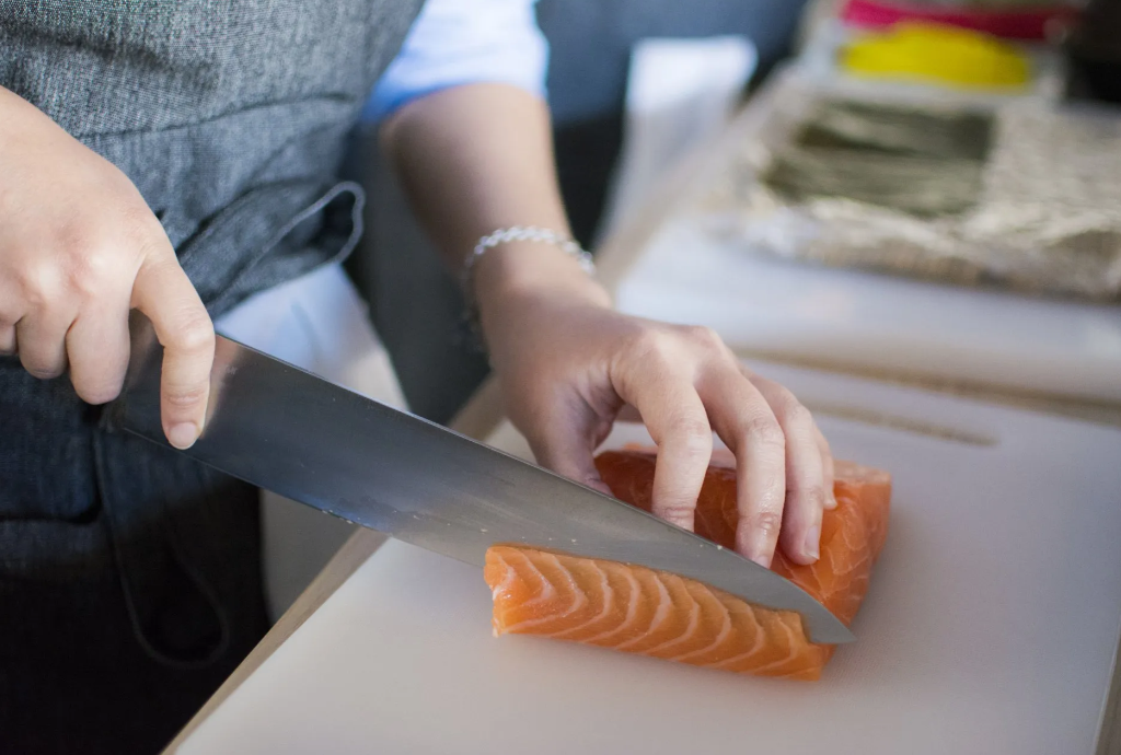 Mani che affettano il salmone su un tagliere con un coltello