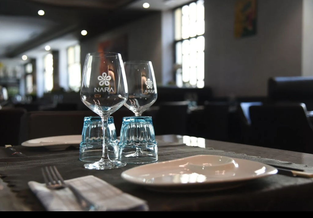 Elegante apparecchiatura da ristorante con bicchieri da vino, piatti e posate in una sala da pranzo illuminata da luci soffuse.