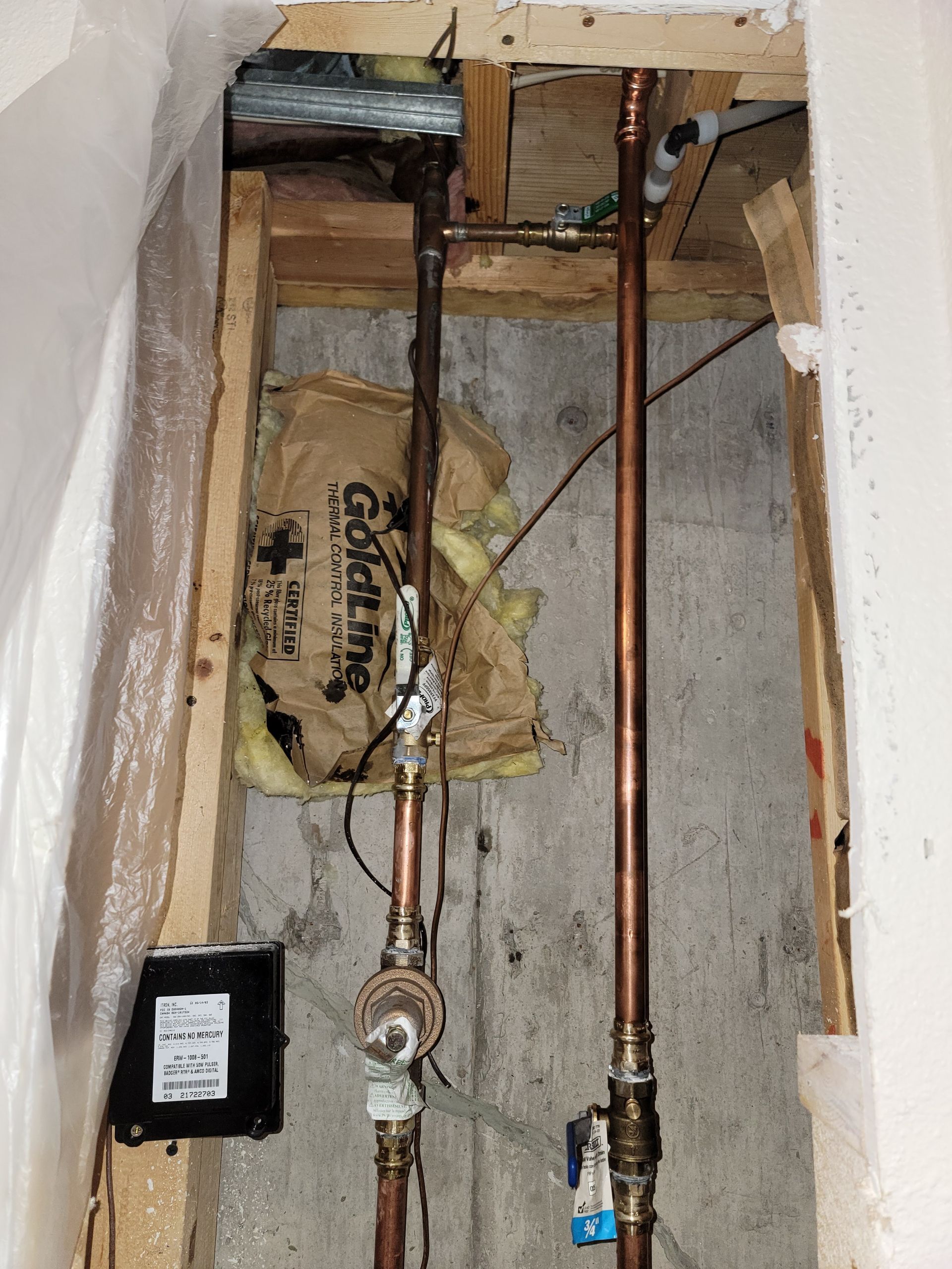 Copper pipes in a wooden frame. Includes a gas meter, wiring, and insulation against a concrete wall.