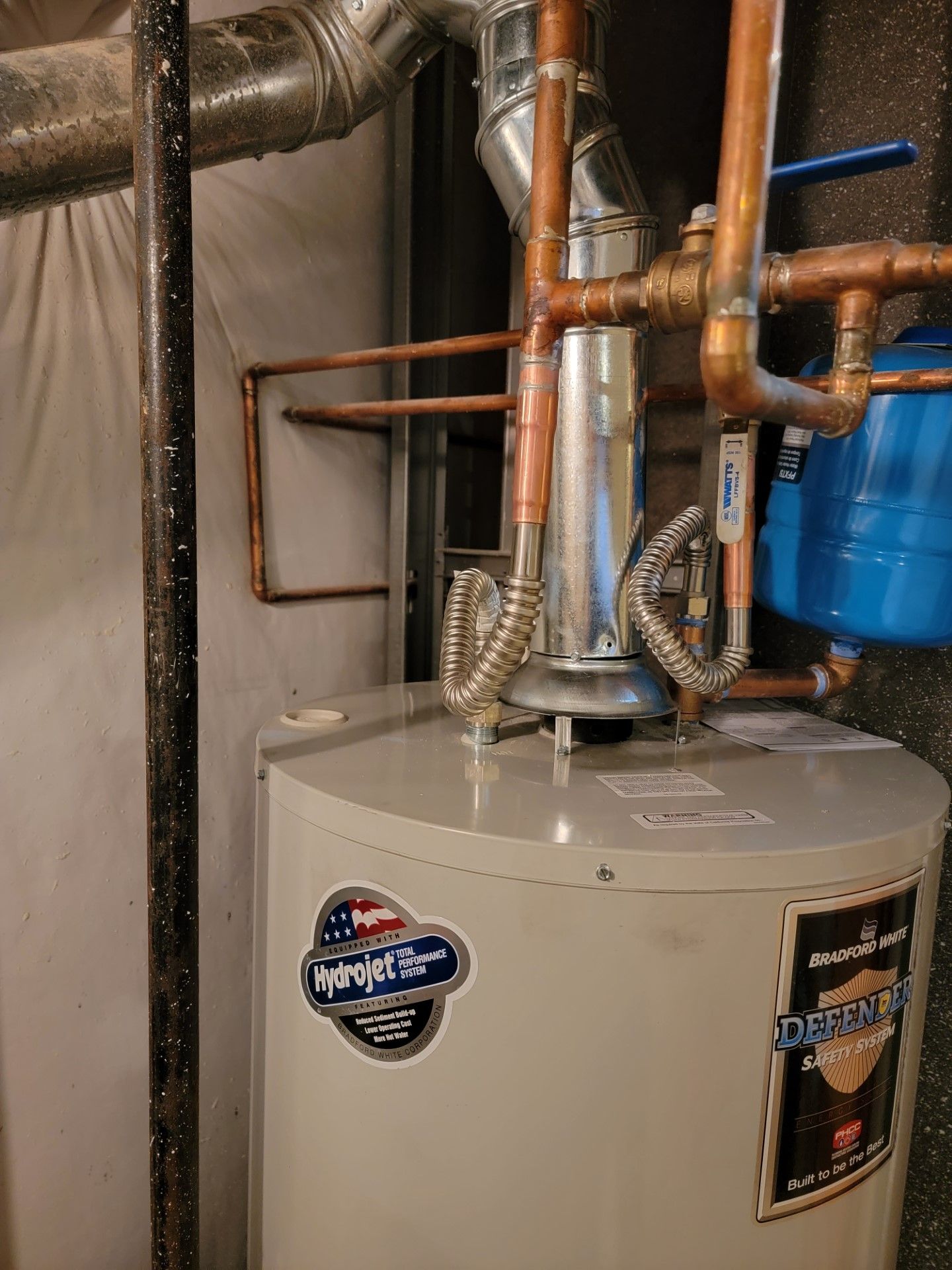 A water heater with copper pipes in a utility room. Blue expansion tank on the right.