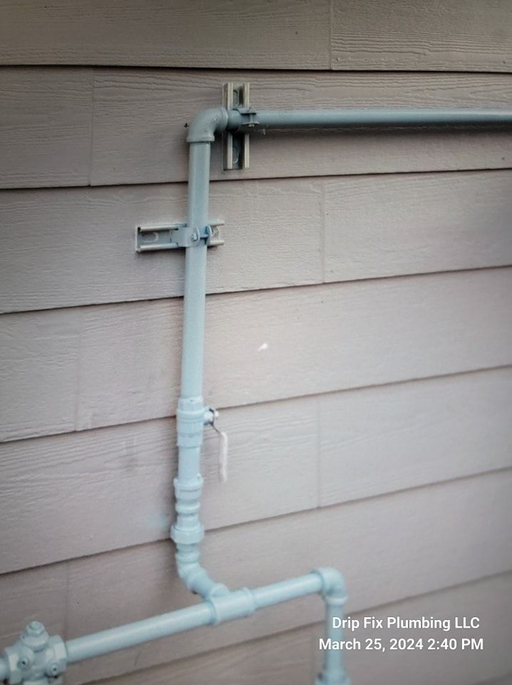 Gray gas pipes with a shutoff valve attached to a beige siding wall, supported by metal brackets.
