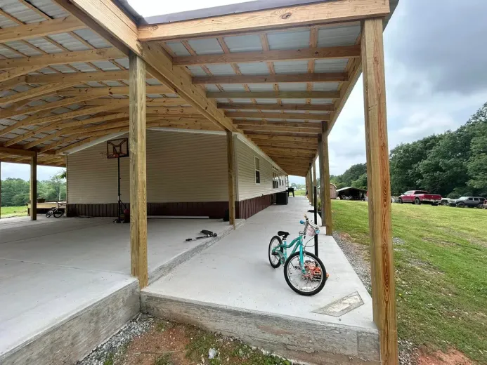 Covered concrete porch alongside a tan mobile home, with a bicycle. Outdoors, cloudy day.