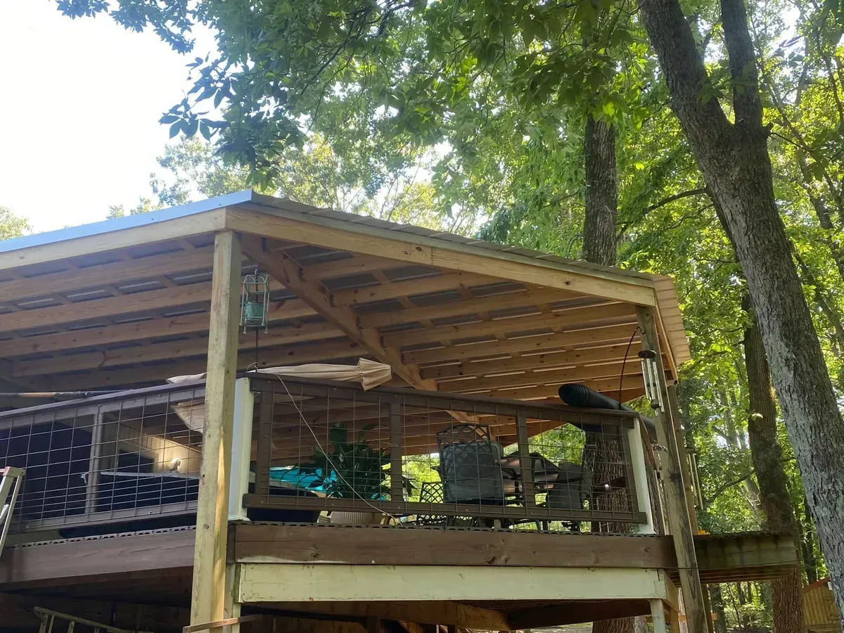 Wooden deck with a covered roof, surrounded by trees in a natural setting.