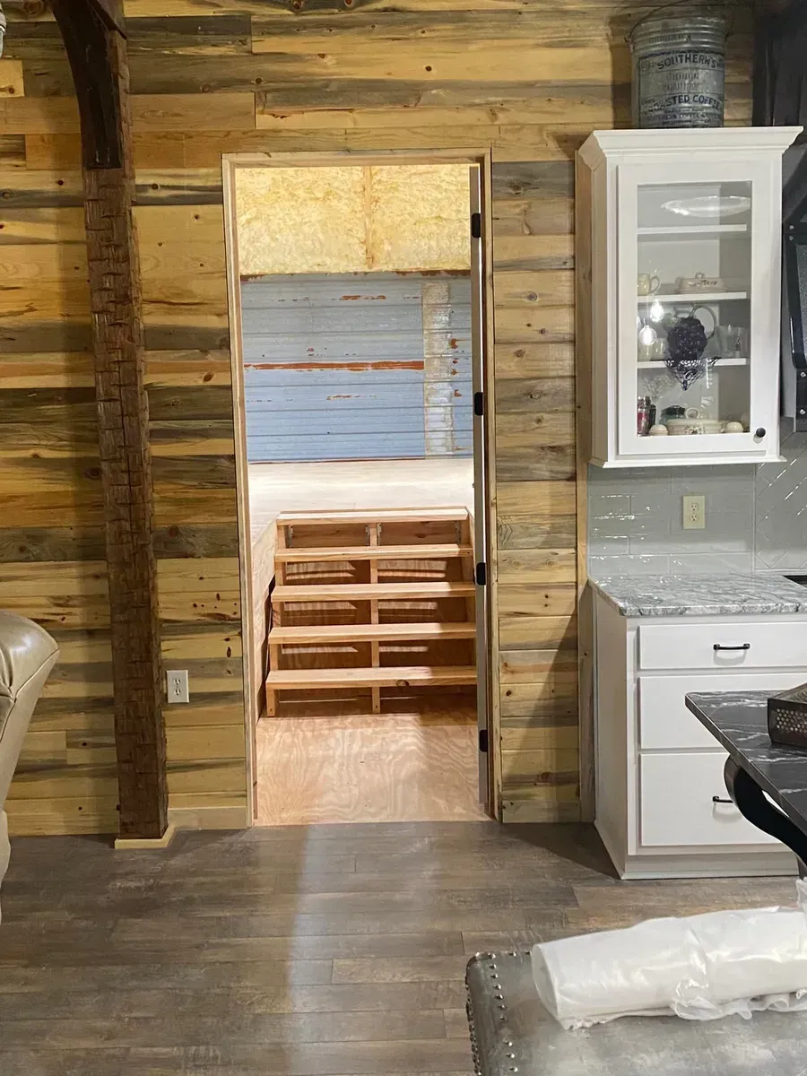 Interior view with wooden walls, doorway leading to stairs. White cabinets, countertop, and a gray floor.