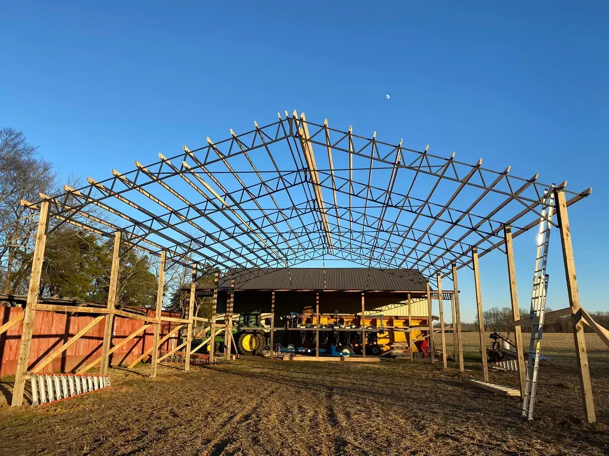 Wooden barn frame under construction on a farm, blue sky overhead.