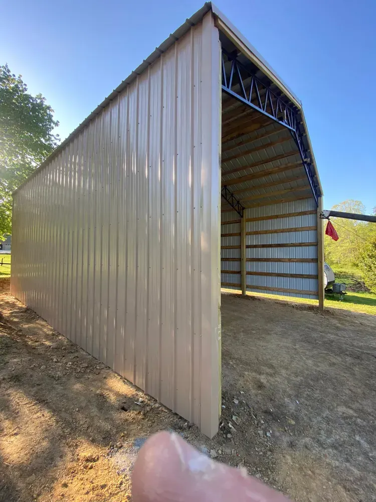 Tan metal shed with open side on a dirt lot, under a blue sky.