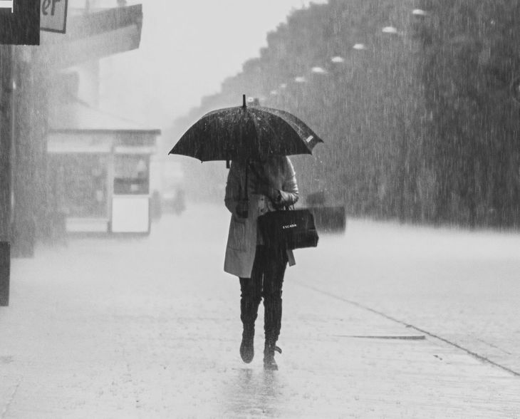 A woman  using an umbrella while walking in the rain on a street sidewalk