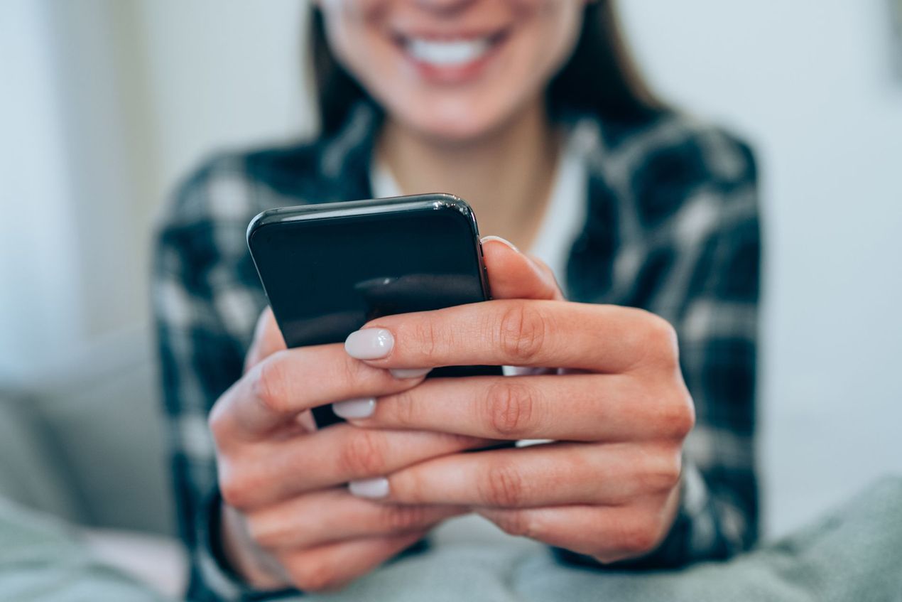 A woman is holding a cell phone in her hands and smiling.