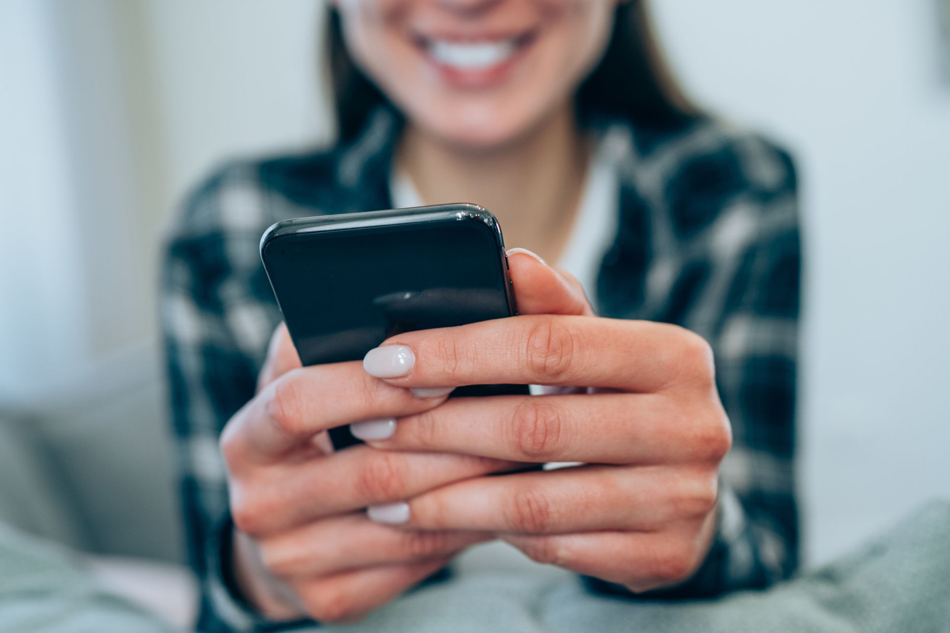 A woman is holding a cell phone in her hands and smiling.