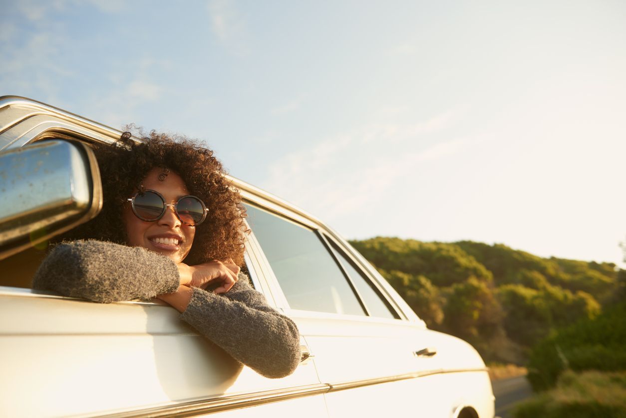 A woman wearing sunglasses is leaning out of the window of a car.