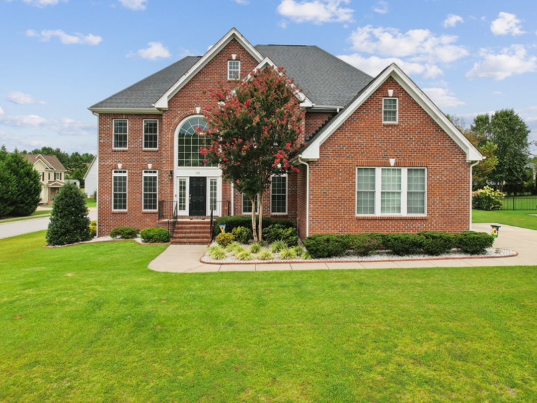 Brick house with a dark roof, arched window, and green lawn.