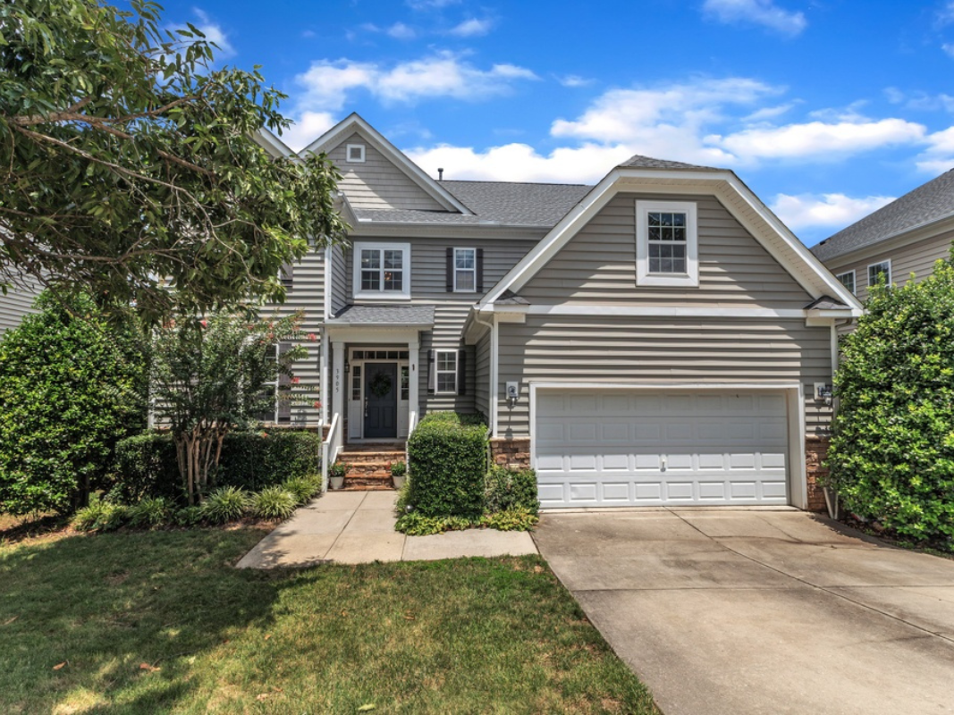 Gray house with white garage door, green lawn, and blue sky.