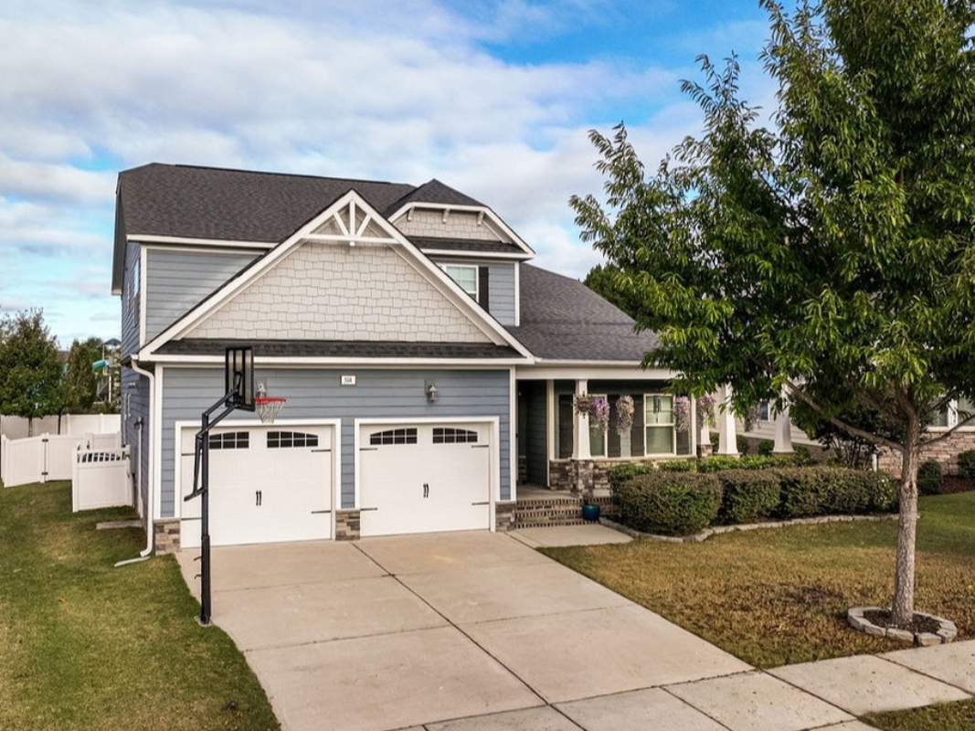 Gray house with white garage door, green lawn, and blue sky.