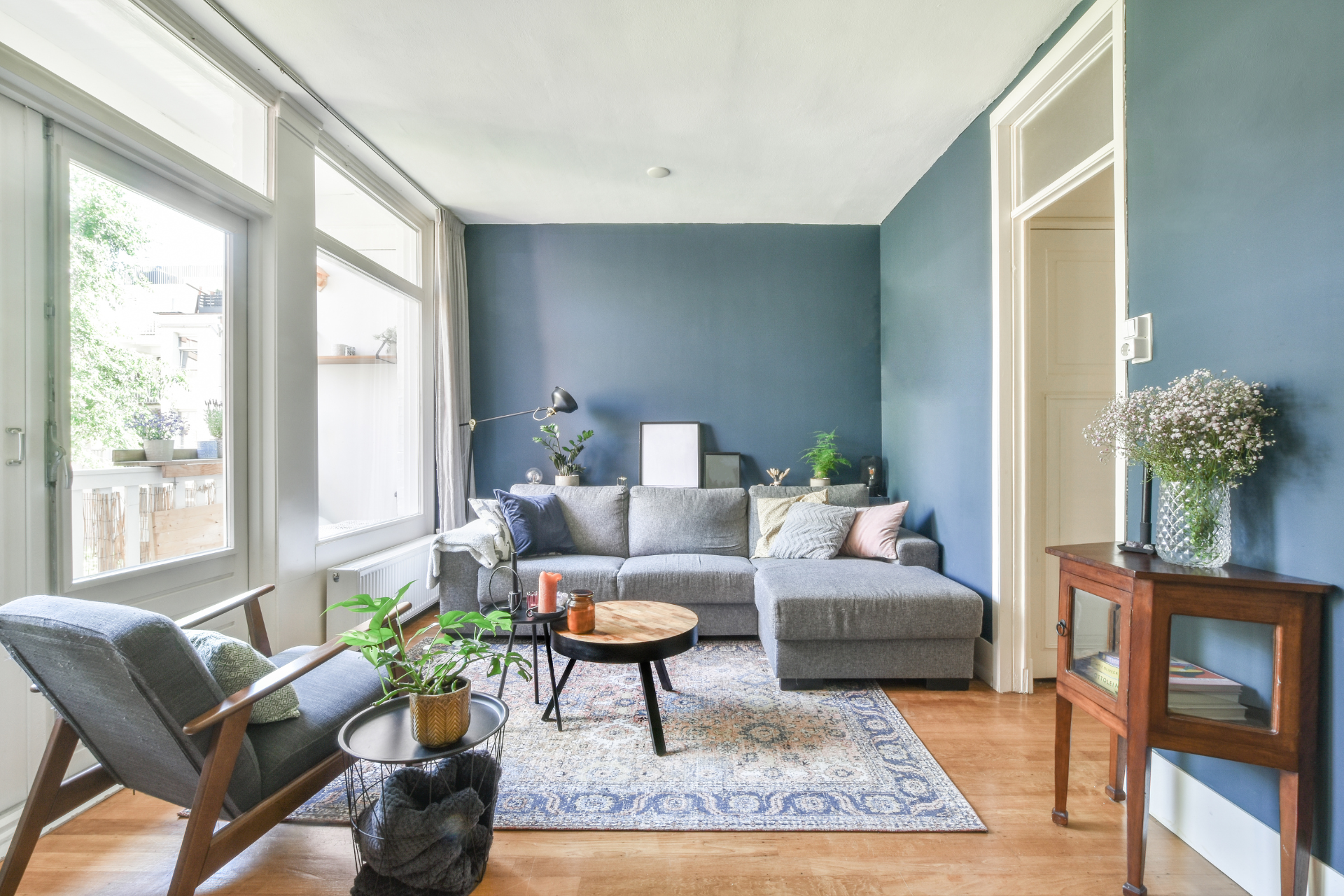 Living room with blue walls, gray sectional, rug, chair by window, and small table.