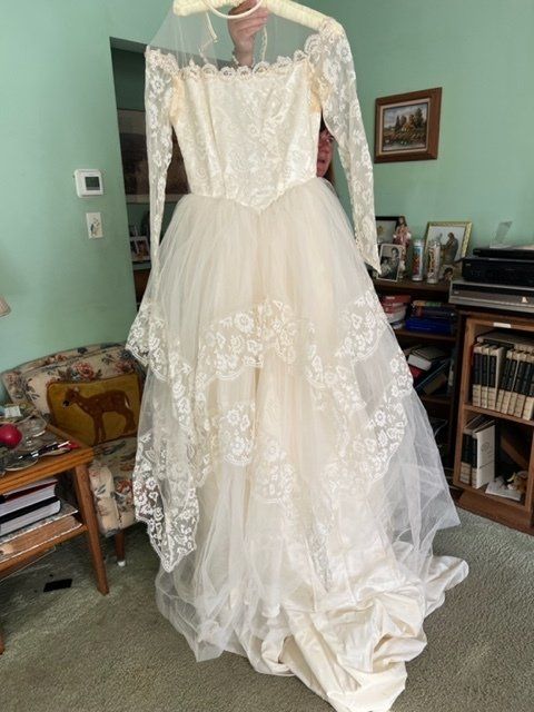 A white lace wedding dress is hanging on a hanger in a living room