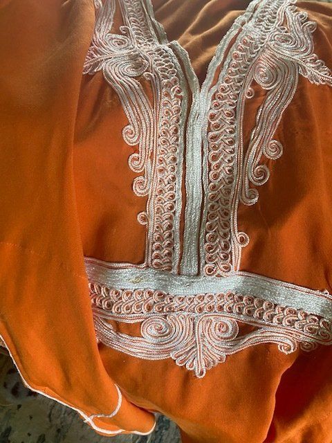 A close up of a piece of orange fabric with white embroidery