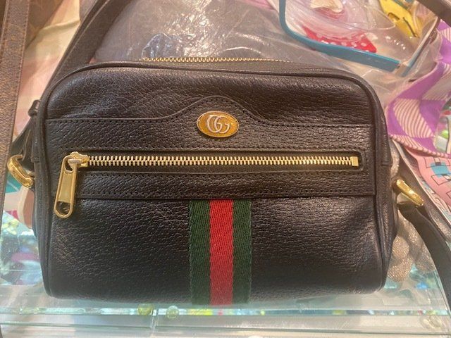 A black purse with a red , green and white stripe on the side is sitting on a glass shelf.