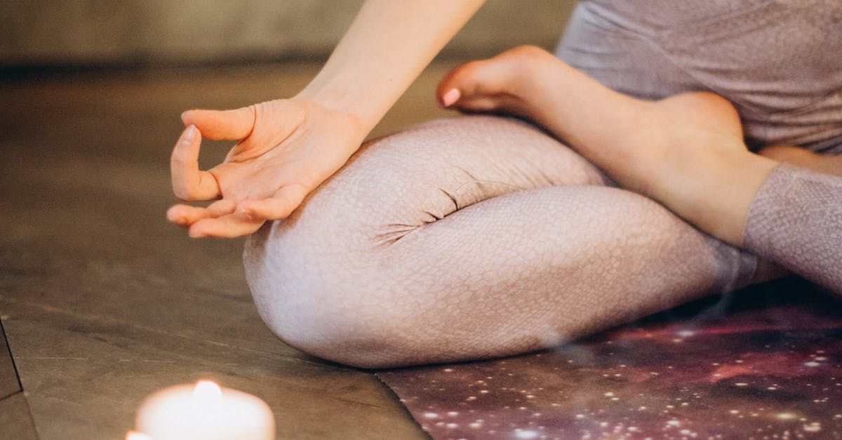 A woman is sitting on a yoga mat next to a candle.