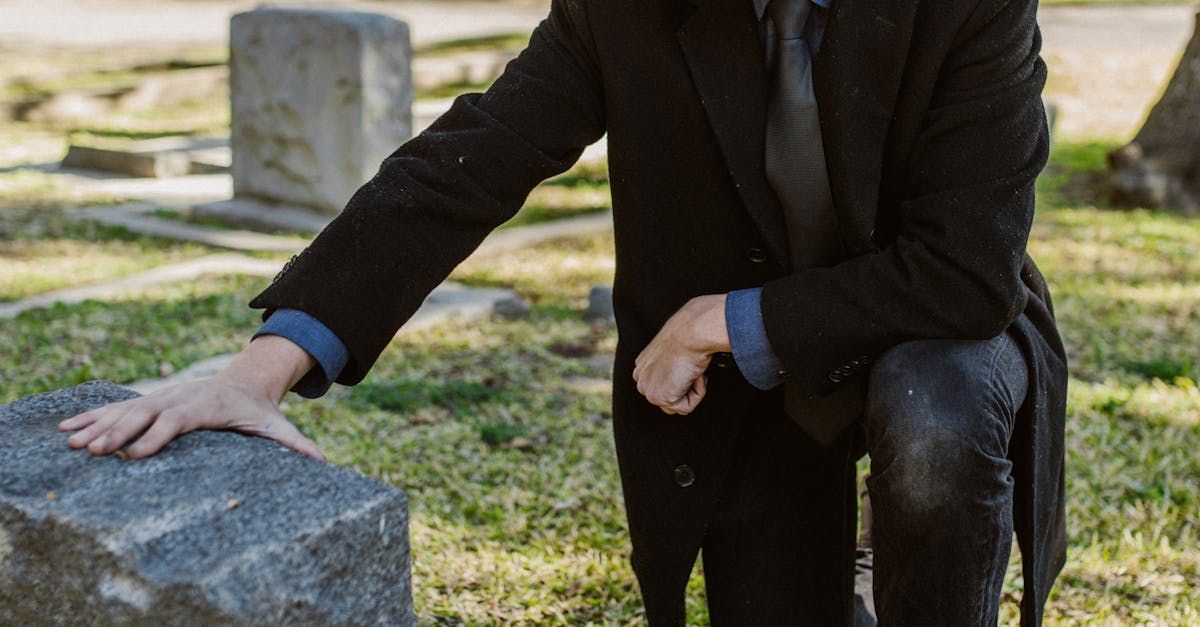 A man in a suit and tie is kneeling in front of a grave in a cemetery.