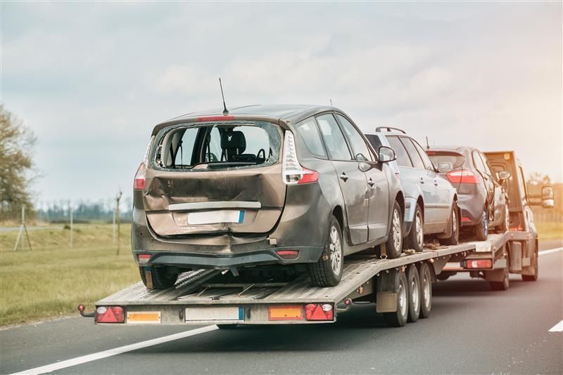 Cars damaged in a collision on a tow truck, driving on the road.