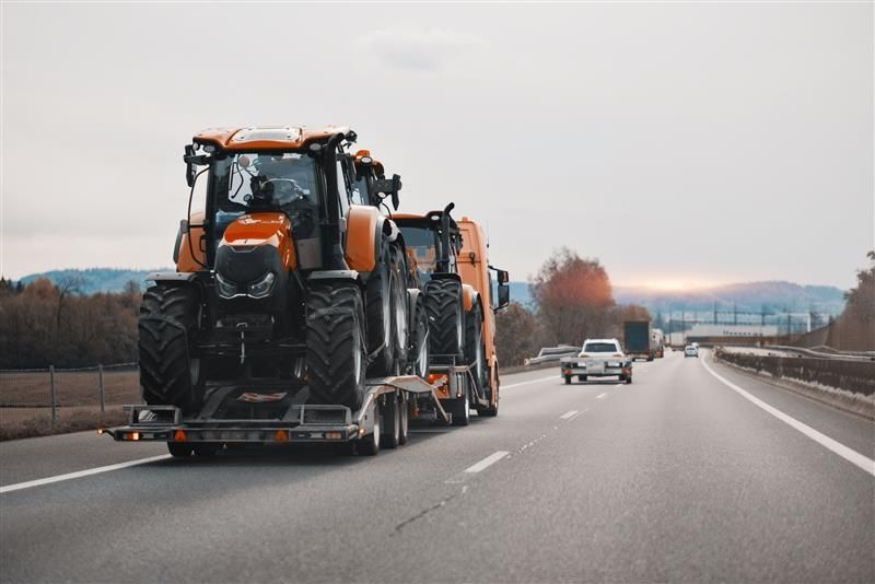 Orange tractor on a trailer being transported on a highway, likely to a farm.