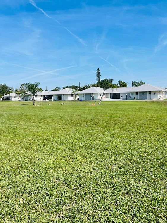 Green lawn in front of a row of white buildings under a bright blue sky with a few wispy clouds.