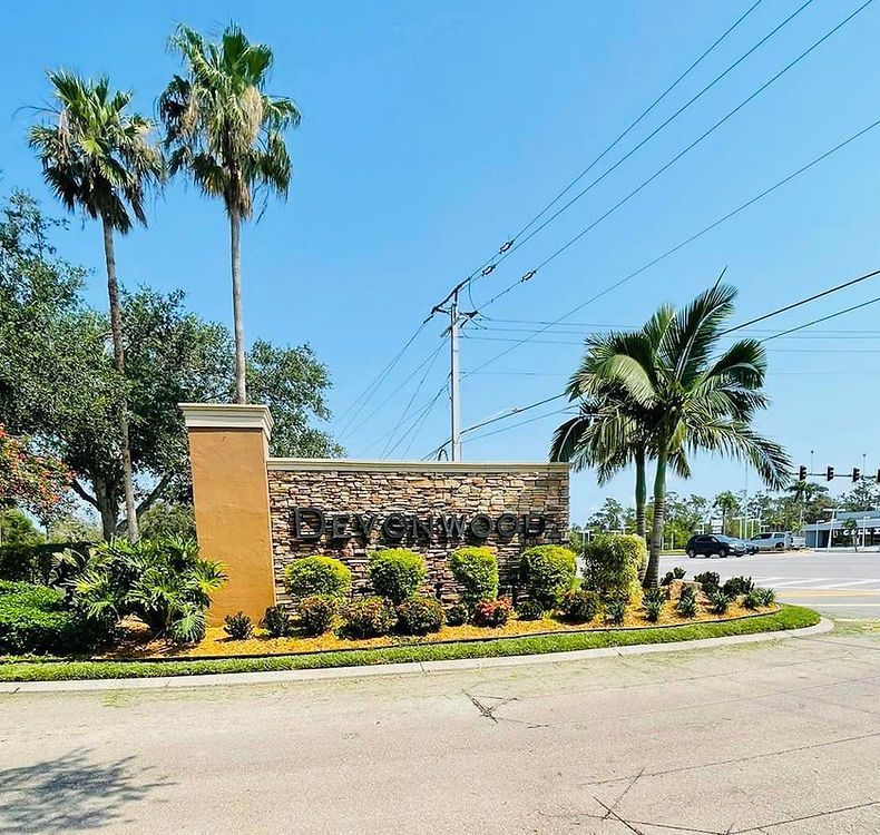 Sign for Bayshore Woods subdivision with palm trees, lush landscaping, and clear blue sky.