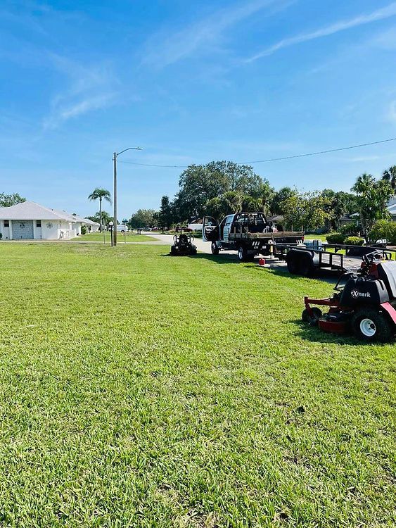 Lawn care equipment parked on a green lawn near a residential area on a sunny day.