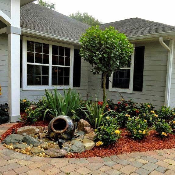 Landscaped front yard with a decorative stone fountain and various plants, including a small tree.