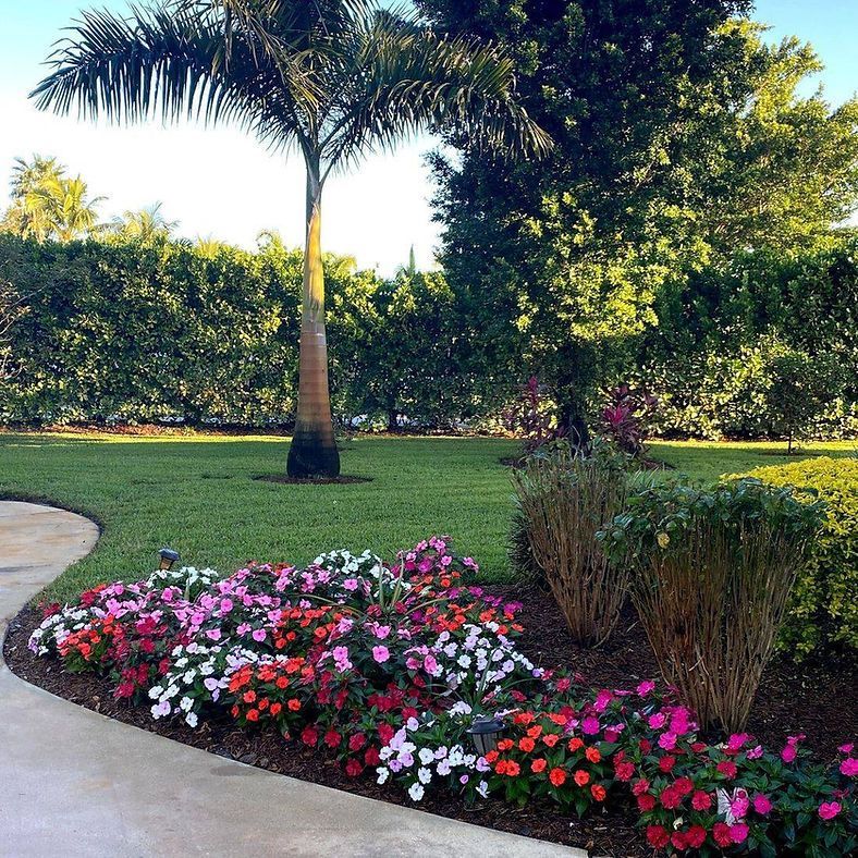 A vibrant garden bed curves alongside a concrete path bursting with colorful flowers.