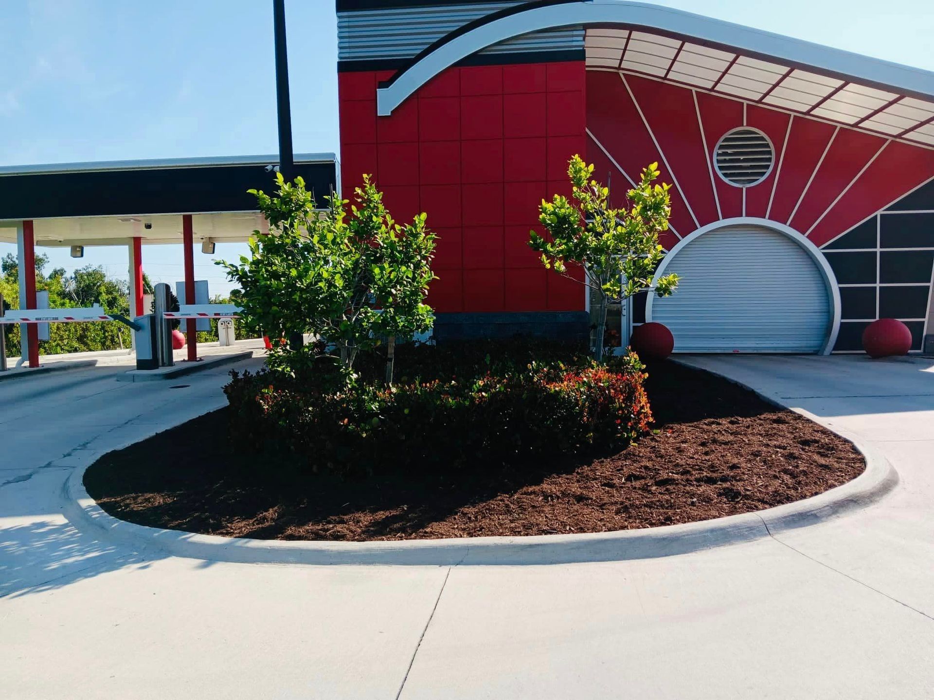 Exterior of a red car wash with a small landscaped island in the foreground.