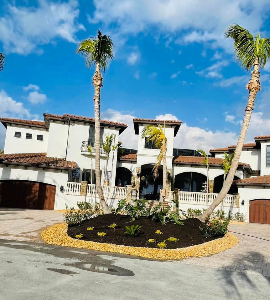 Luxury home with white stucco walls, red-tiled roof, palm trees, and a circular driveway on a sunny day.