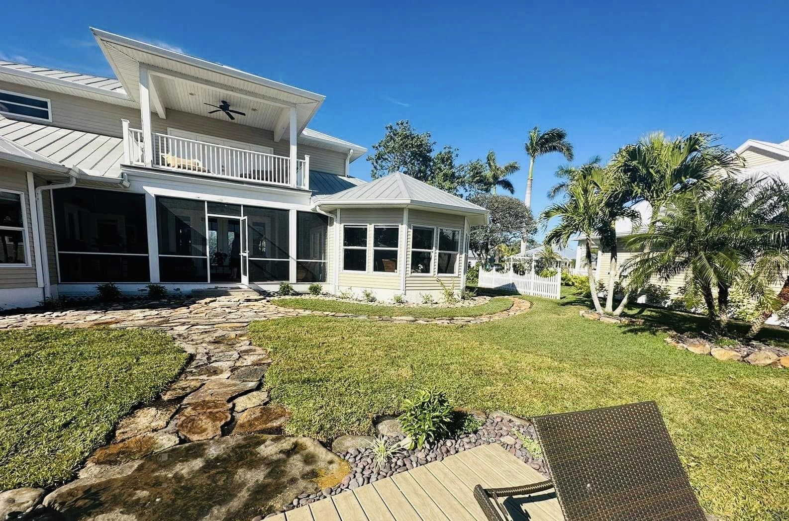 Backyard of a multi-story house with a screened porch and a view of palm trees under a clear blue sky.