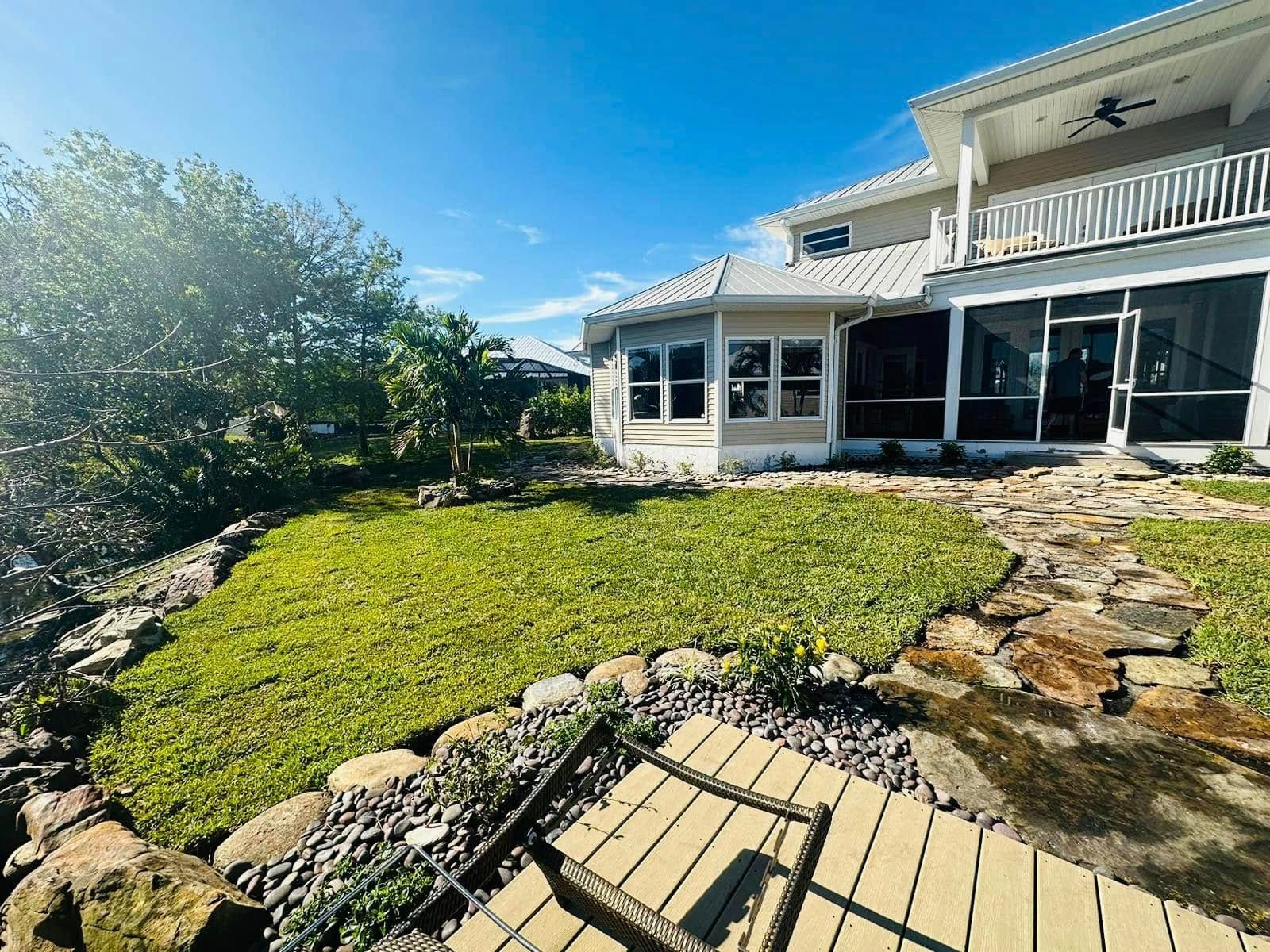 A coastal house with a green lawn and stone path leading to the screened porch, under a blue sky.