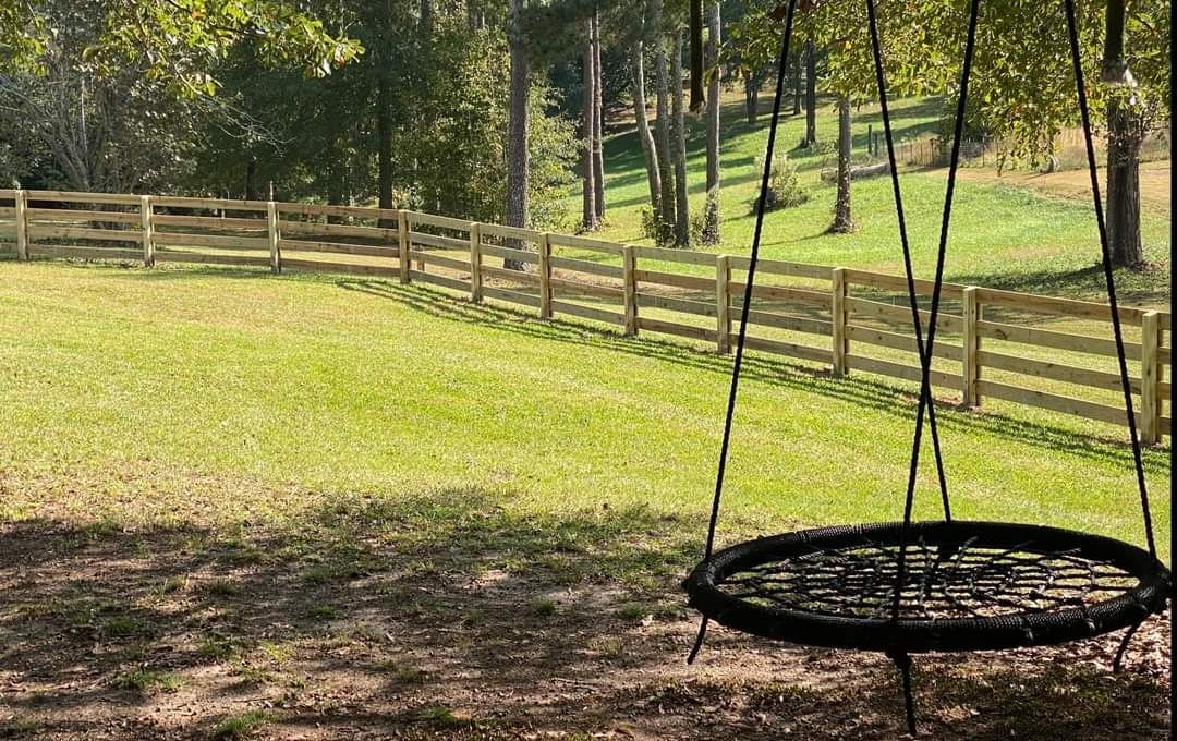 A round swing is hanging in the middle of a grassy field.