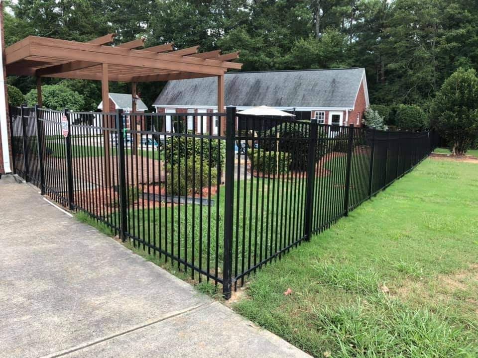 A black fence surrounds a lush green yard in front of a house.