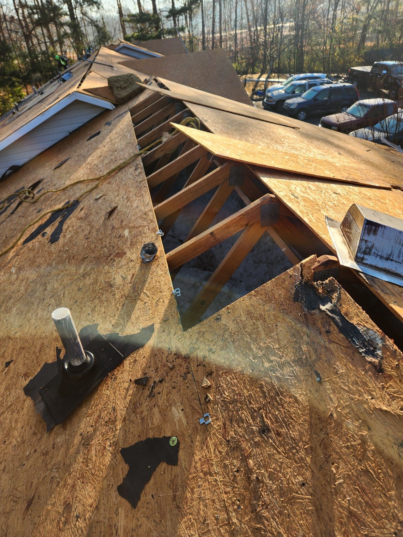 A close up of a roof under construction with cars parked in the background.