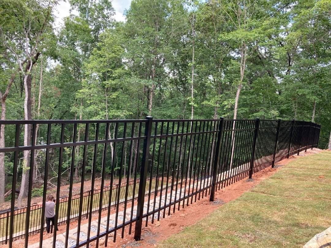 A black metal fence surrounds a grassy area with trees in the background.