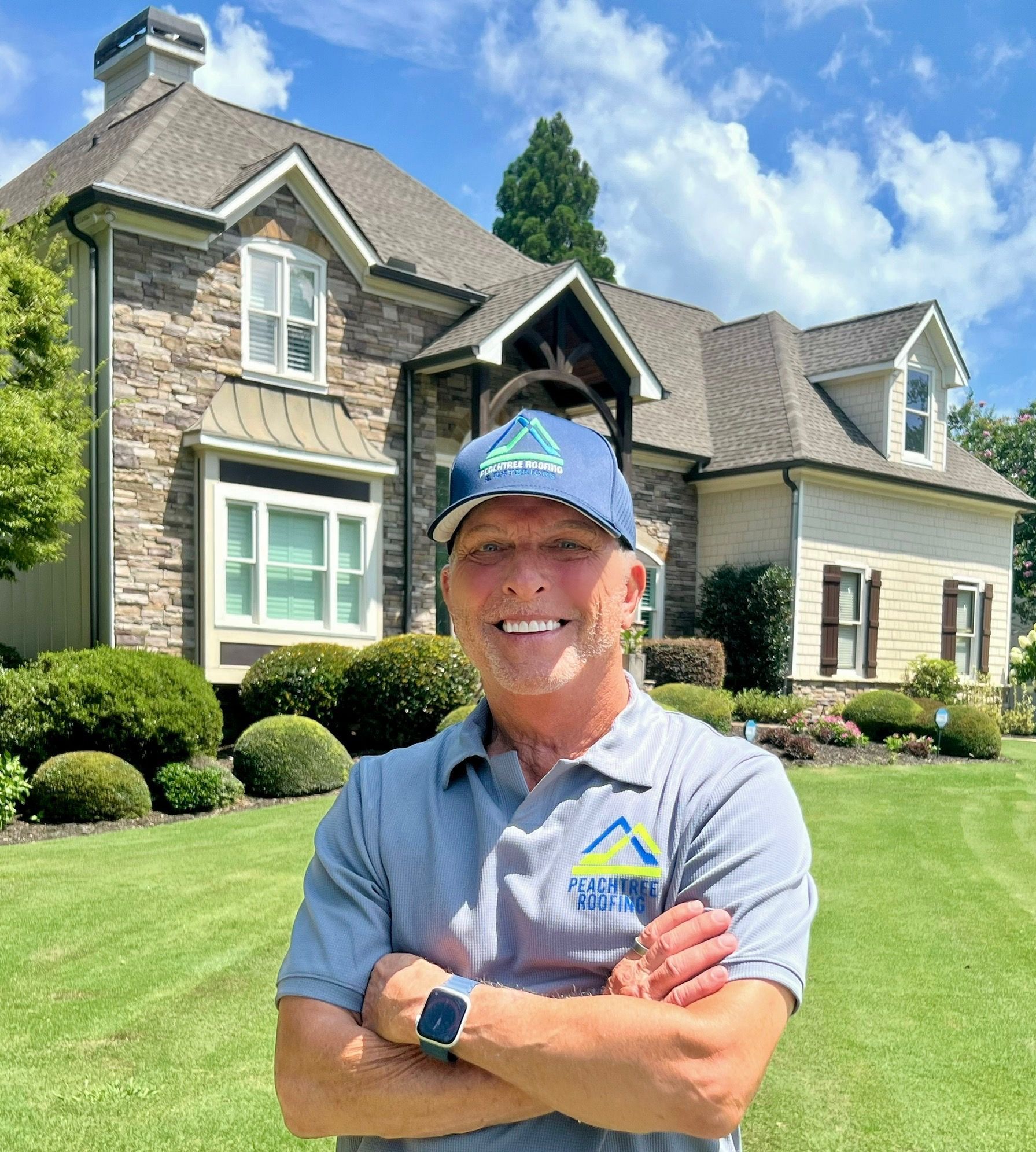 A man is standing in front of a large house with his arms crossed.