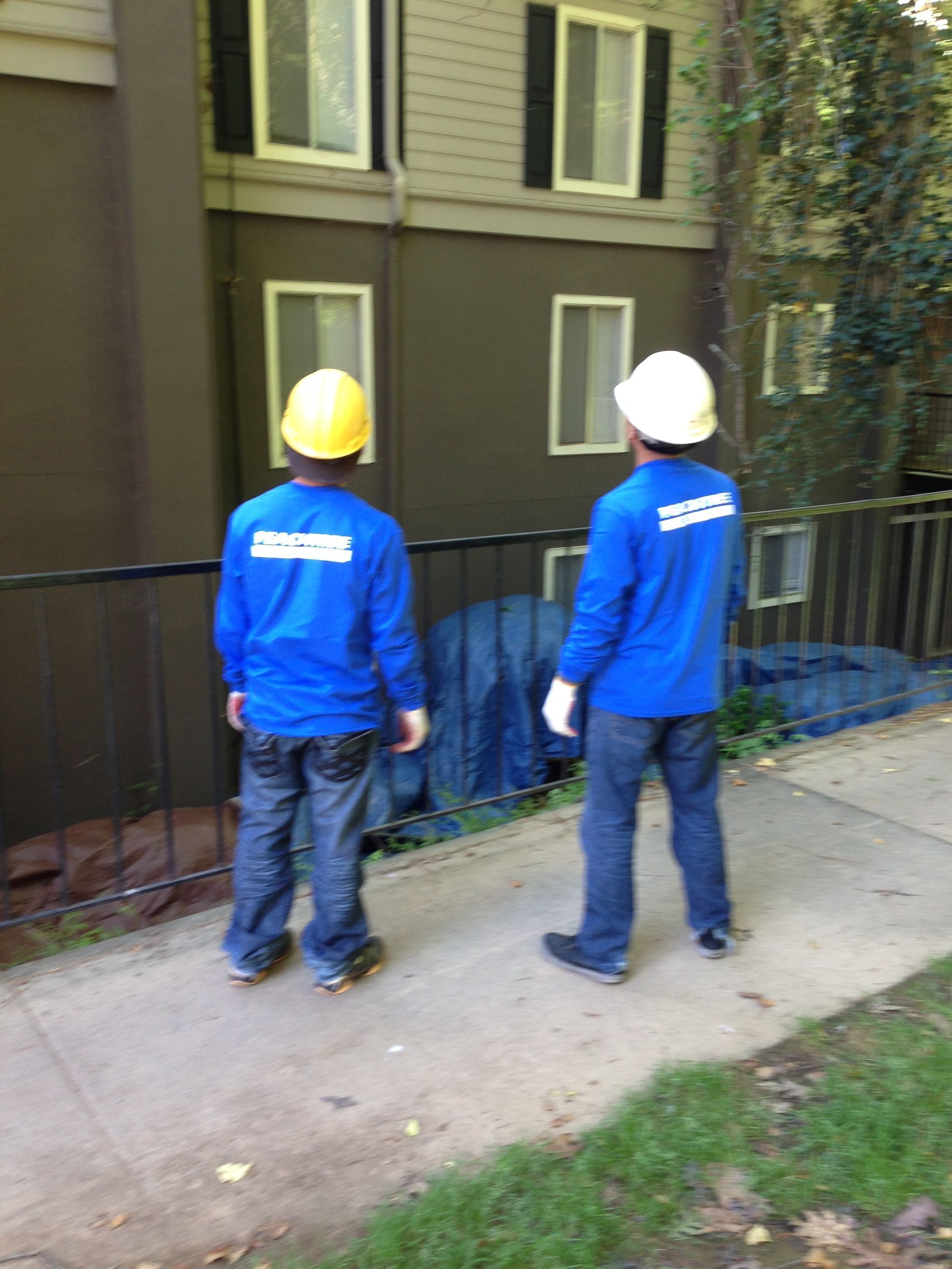 Two men wearing hard hats are standing in front of a building.