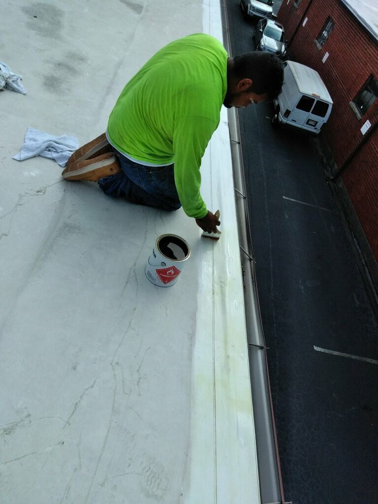 A man in a green shirt is kneeling on a roof with a bucket of paint.