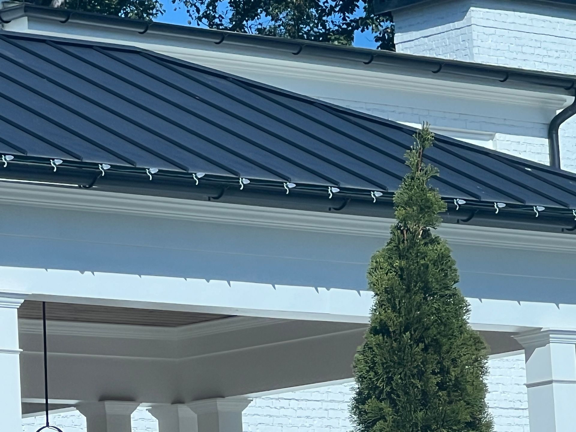 A white house with a black roof and a tree in front of it.