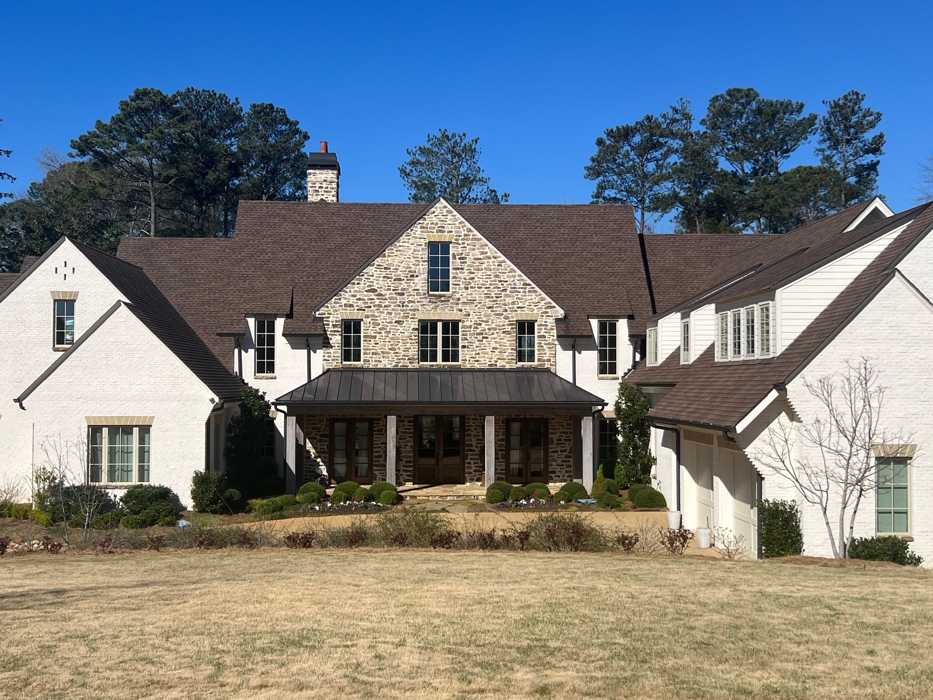 A large white house with a brown roof is sitting in the middle of a grassy field.