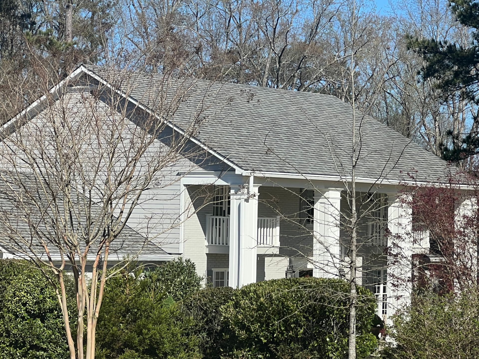 A white house with a gray roof is surrounded by trees and bushes.
