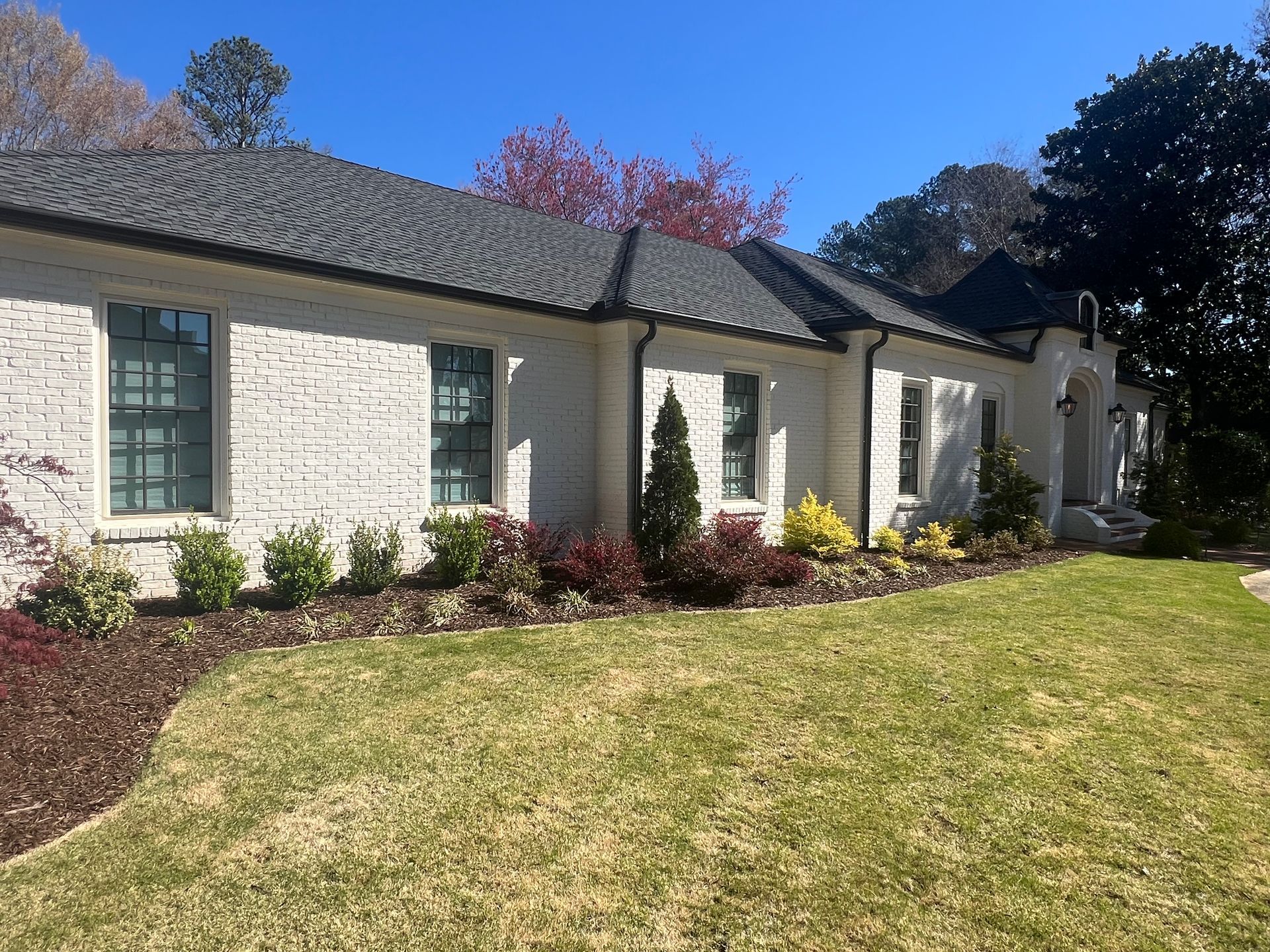 A large white brick house with a lush green lawn in front of it.