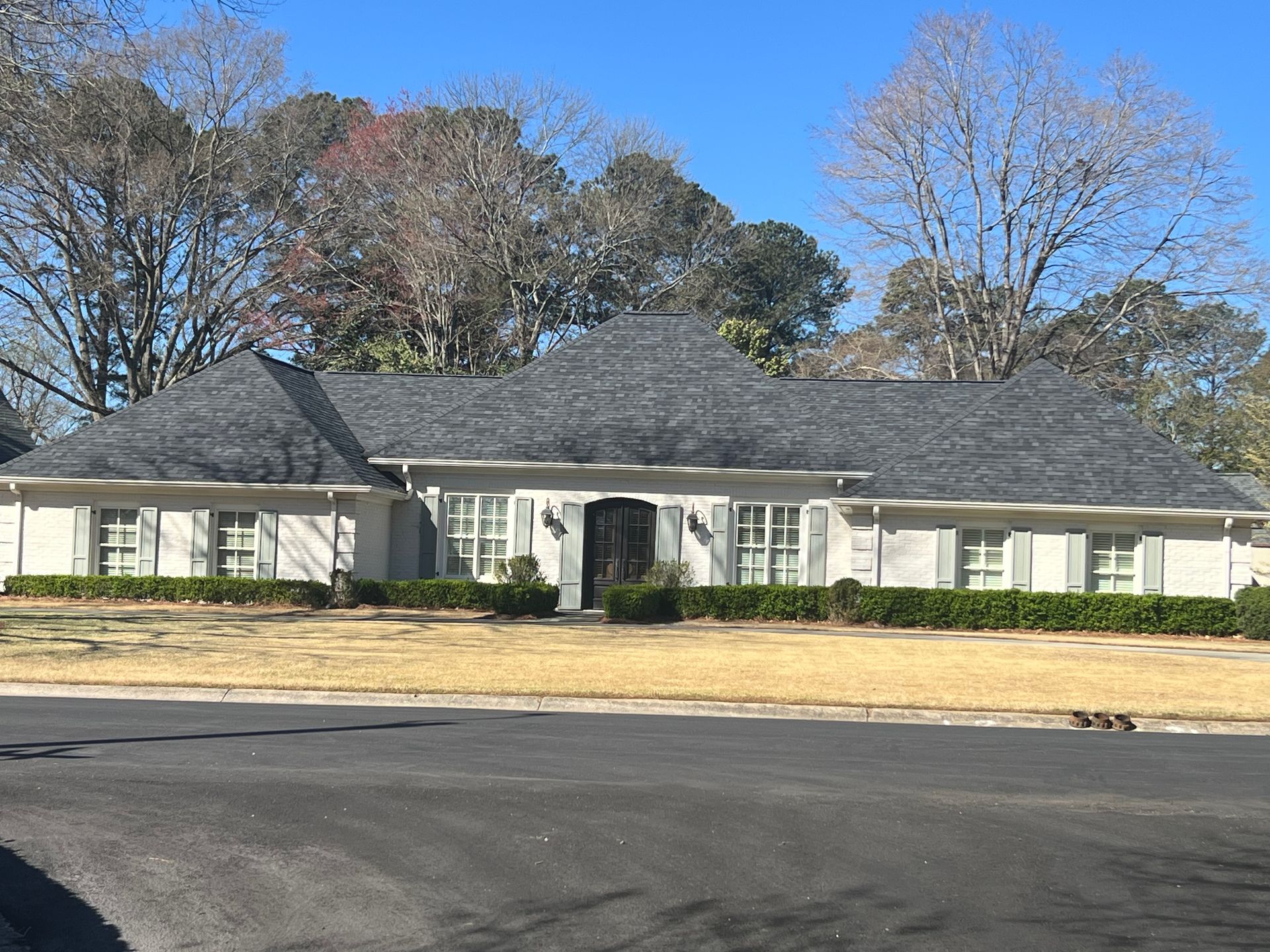 A large white house with a gray roof and trees in the background.