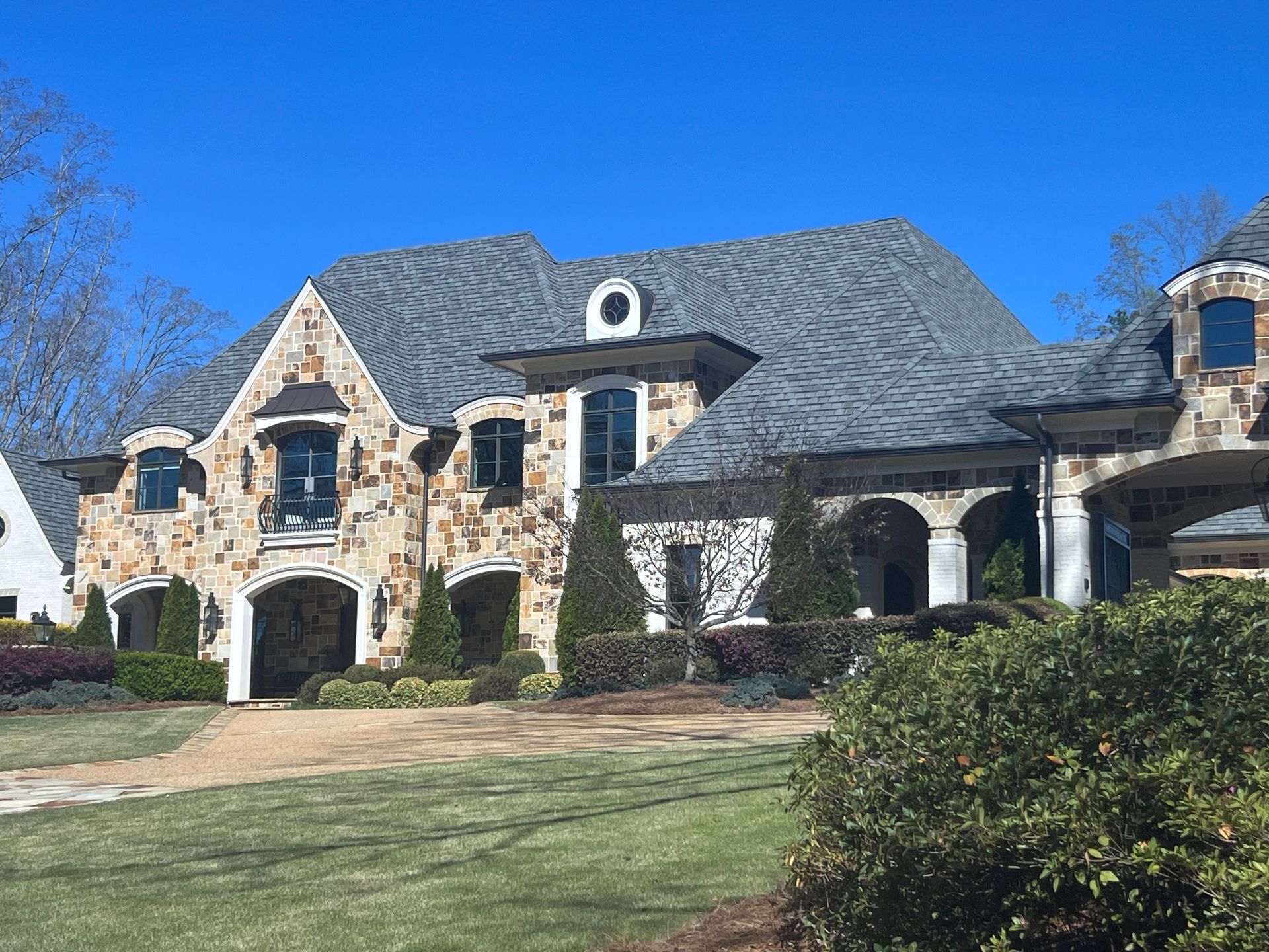 A large house with a gray roof is sitting on top of a lush green field.