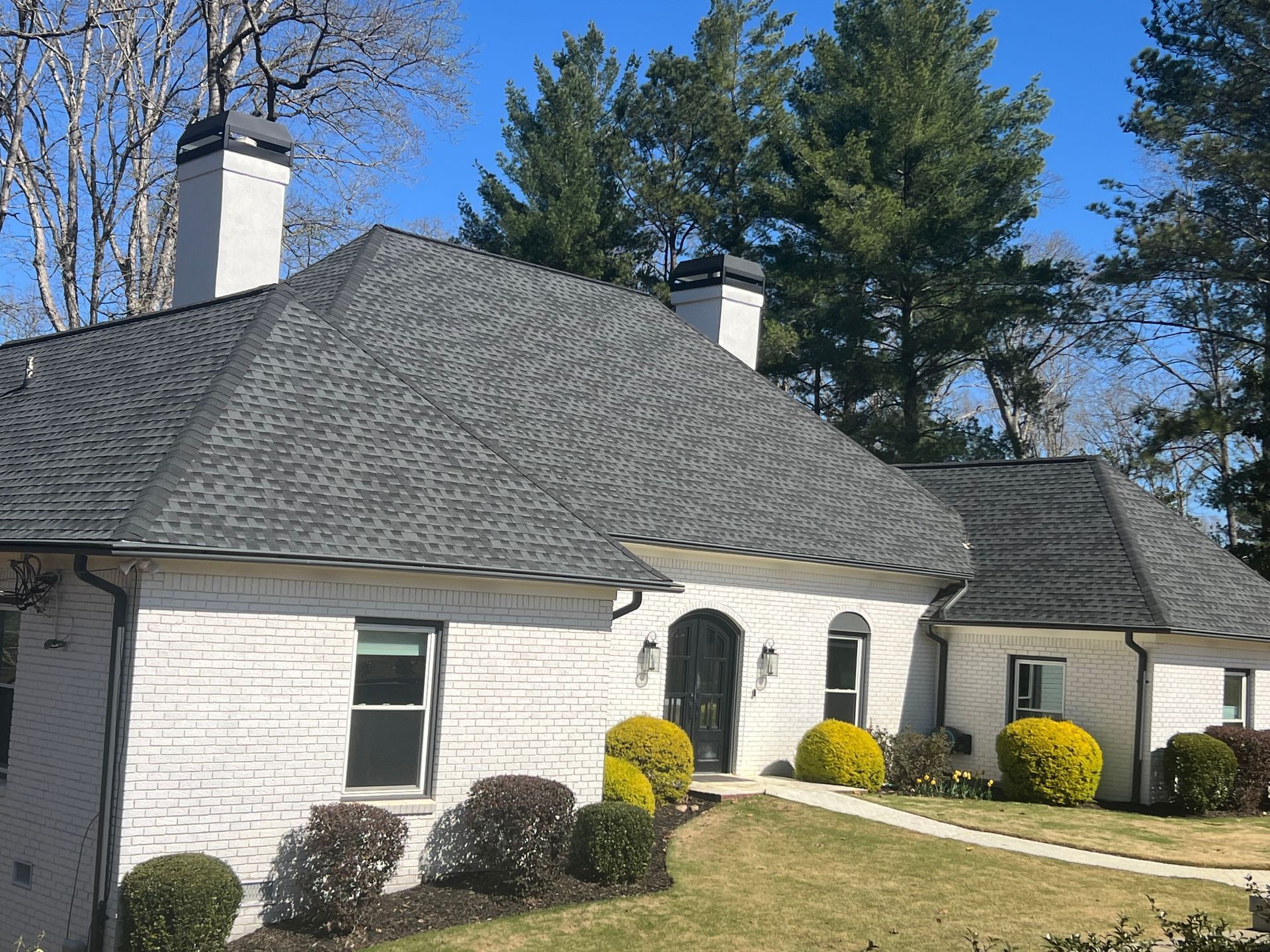 A white brick house with a gray roof and chimneys
